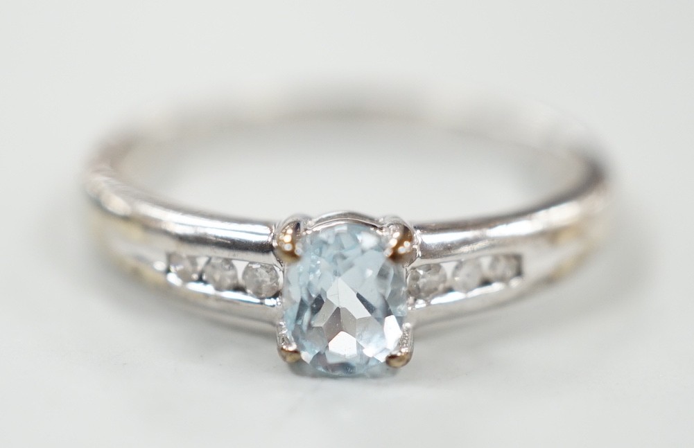 A modern 9ct white gold and oval cut blue topaz ring, with diamond chip set shoulders, size N, gross weight 2 grams.